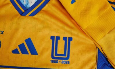 El diseño mantiene el amarillo vibrante tradicional con detalles en azul, incluyendo un cuello en “V” y una franja central dinámica que conecta con líneas laterales.