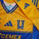 El diseño mantiene el amarillo vibrante tradicional con detalles en azul, incluyendo un cuello en “V” y una franja central dinámica que conecta con líneas laterales.