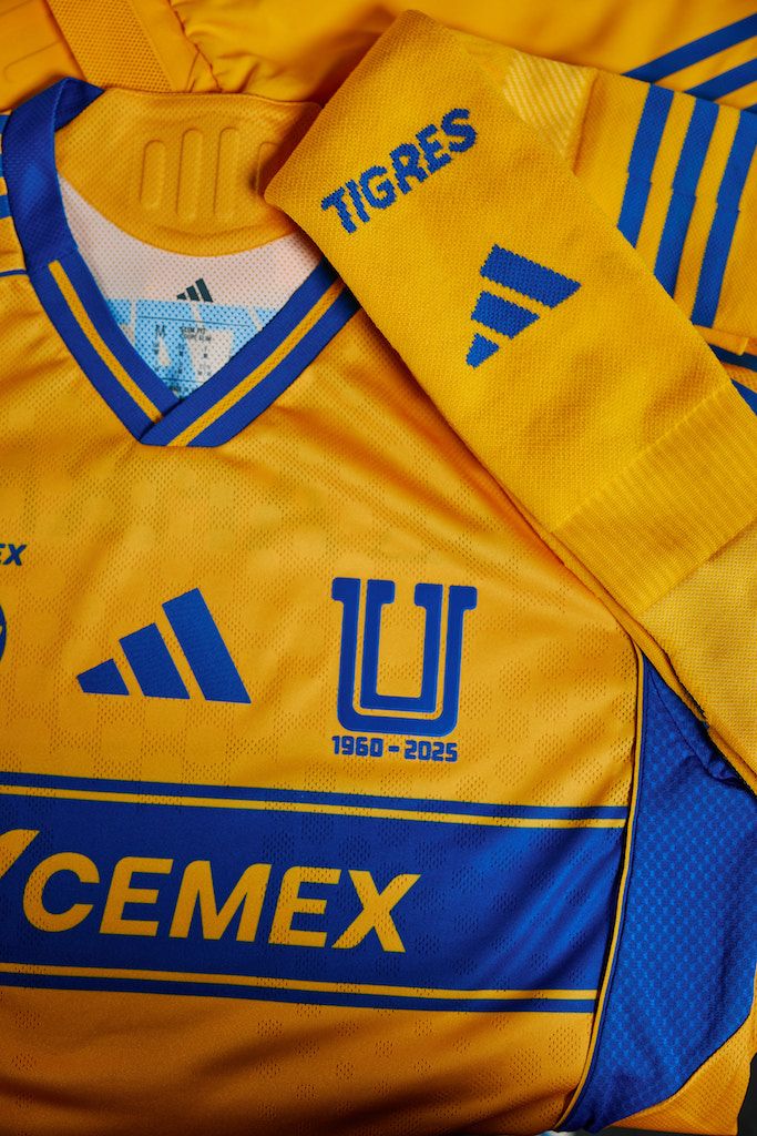 El diseño mantiene el amarillo vibrante tradicional con detalles en azul, incluyendo un cuello en “V” y una franja central dinámica que conecta con líneas laterales.